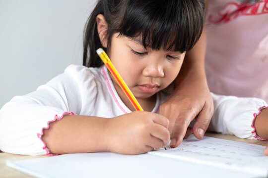 Asian girls aged 4-5 are having mom help with homework, kids holding pencils and writing homework.