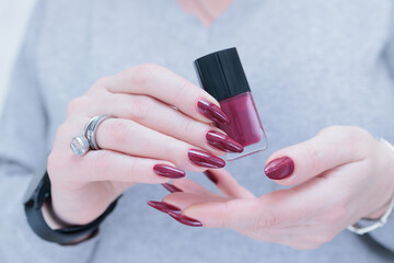 Woman hand with long nails and a bottle of dark red burgundy nail polish