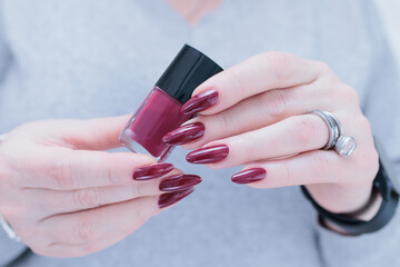 Woman hand with long nails and a bottle of dark red burgundy nail polish