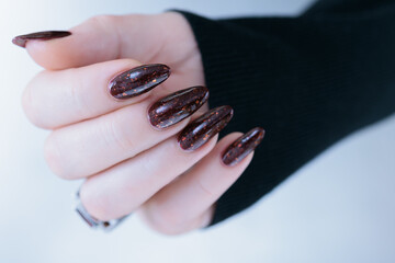 Woman hand with long nails and a bottle of dark red burgundy nail polish