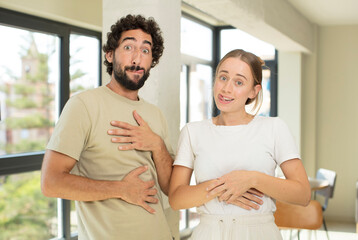 young adult couple with a goofy, crazy and surprised expression, feeling stuffed, fat and full of food