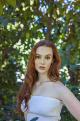Naklejka premium very beautiful freckled white woman with long red hair in a garden of green leaves