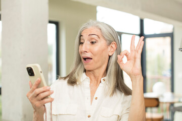 pretty senior woman feeling happy, showing approval with okay gesture. smartphone concept