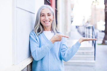 senior retired pretty white hair woman smiling, feeling happy, carefree and satisfied, pointing to concept or idea on copy space on the side