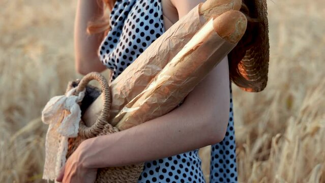 woman in wheat field,with baguette bread in bag and brown paper at sunset golden hour.woman raising up hand,wearing large sun beach hat,wide brim, on back.touching with hand wheat ears.4k