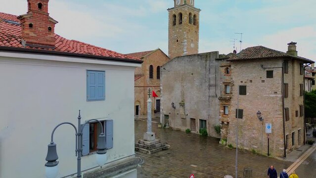 Aerial view of the old city. Roofs of buildings with red tiles and many chimneys. The bell tower of the Catholic Cathedral in the city center. Traveling through narrow streets. Italy Grado 07.2023