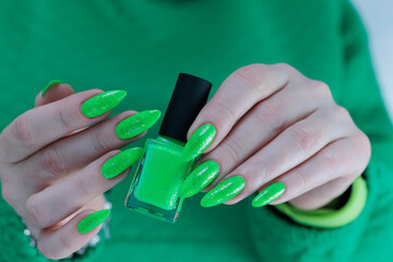 Female hand with long nails and neon green manicure with bottles of nail polish