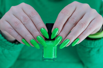 Female hand with long nails and neon green manicure with bottles of nail polish