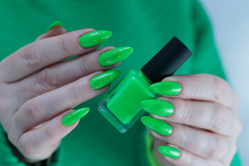Female hand with long nails and neon green manicure with bottles of nail polish