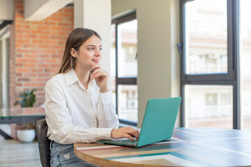 young pretty woman smiling with a happy, confident expression with hand on chin. working with a laptop