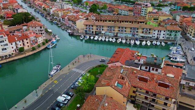 Aerial view of the sea water canal in the city center where fishing boats and amateur sailing yachts are moored. Small classic fishing boats with nets. Little Venice. Grado Italy 07.2023