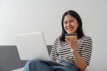 Happy young attractive woman shopping online via laptop computer, using credit card at home