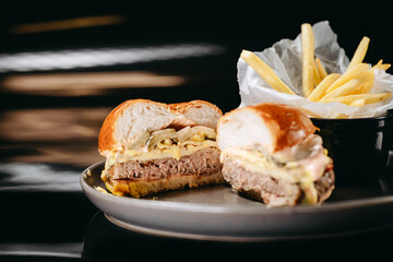 Sliced cheese burger with bacon and fries on a black background