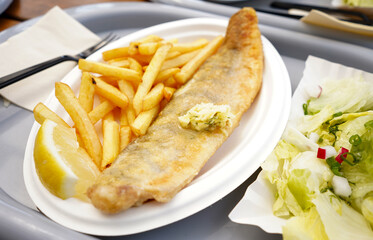 Fish and chips on a plate. Fried fish with butter on it and french fries on plastic plate in restaurant