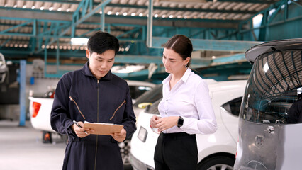 Professional mechanic in a suit working in a garage The mechanic talks to the customer and agrees to fix the car successfully. Send contract to pick up the car. The two shook hands with satisfaction.