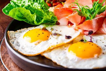 fried eggs with ham, salad and hummus on plate
