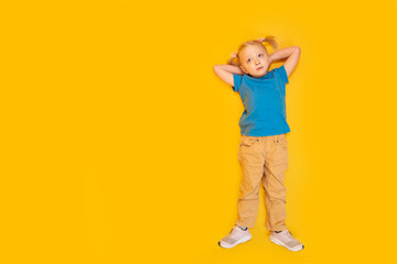 Child lying on yellow background. Little girl with two ponytails wears blue T-shirt and yellow pants. Top view. Copy space, mockup