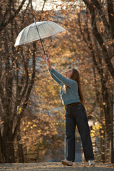 Beautiful young woman fun with transparent umbrella. Happy young woman with long hair in autumn park.