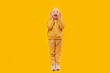 Fototapeta na wymiar Child is surprised or screams. Full-length portrait of preschool girl in yellow suit on yellow background.