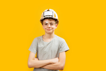 Caucasian teenager boy wears glasses and helmet crossed his arms across his chest and looks into the camera on yellow background. Copy space.