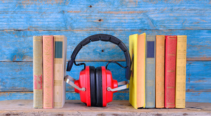 audio book concept with row of books and vintage headphones,blue wooden planks in the back