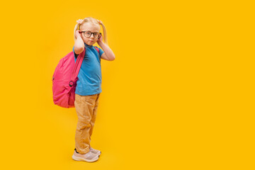 Full length portrait of Serious little blonde girl wearing backpack for school, yellow background . Copy space, mockup