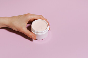 Female hand holding jar of white face or body cream mockup on purple isolated background. Place for your design. Beauty and spa concept