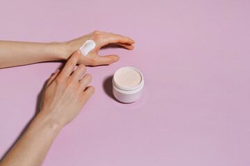 Female hand applying swatch or cream sample to skin from white jar on purple isolated background....