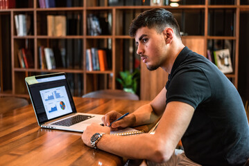 A male college student studying in a university library a young happy man working on laptop with graphs, charts, diagrams on screen in the office workplace.