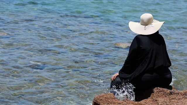 Muslim woman back view wearing black muslim dress and a hat (unrecognizable) sitting by the sea in Egypt