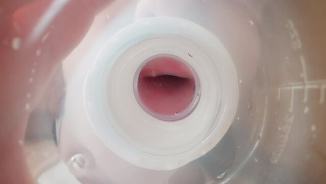 Kid drinks water using white nipple. Little child puts plastic bottle on table and drop runs down. View from inside bottle macro low angle shot