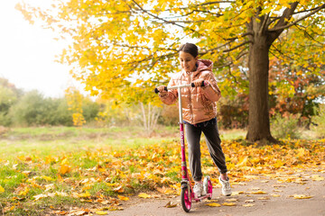 beautiful schoolgirl girl rides a scooter in an autumn park on sunny day