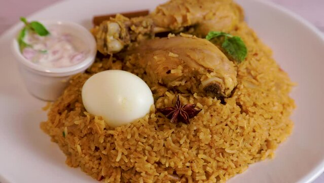 Delicious chicken biriyani on a white plate. Indian style chicken biryani with egg and yogurt.
