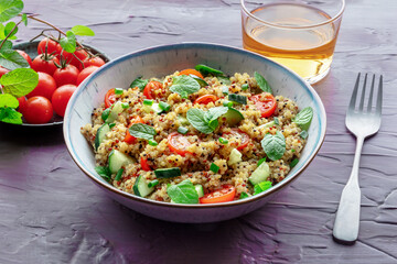 Quinoa tabbouleh salad in a bowl, a healthy dinner with tomatoes and mint on a purple background