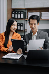 Business documents on office table with tablet and laptop computer and chart and two colleagues discussing data in office.