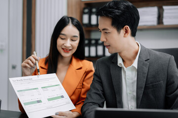 Business documents on office table with tablet and laptop computer and chart and two colleagues discussing data in office.