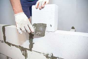 Plastering the wall.Hand holding a spatula with construction mix.Applying putty or tile glue to with lightweight concrete blocks.Plaster the wall with a putty knife.Internal construction