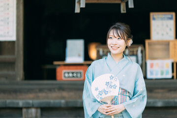 神社の境内でうちわを持つ浴衣姿の日本人女性