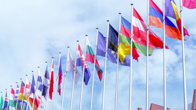 national flags of Europe and other countries on satin flutter in wind in blue sky near building of European Parliament, state symbols, concept of international cooperation, global business
