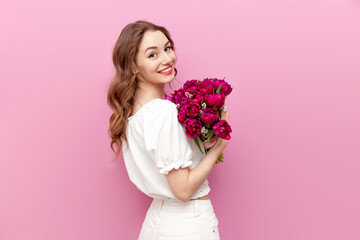 young attractive girl in white clothes holds bouquet of pink tulips and smiles, woman on holiday...