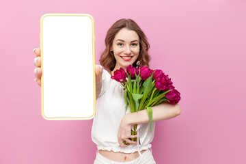 young attractive girl in white clothes holds bouquet of pink tulips and shows blank screen of...