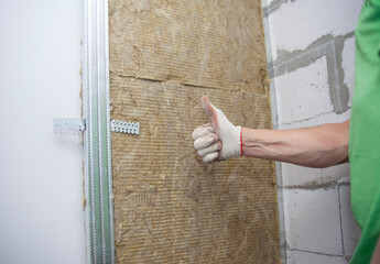 The worker insulates the walls with mineral wool for further cladding with plasterboard. Heat...
