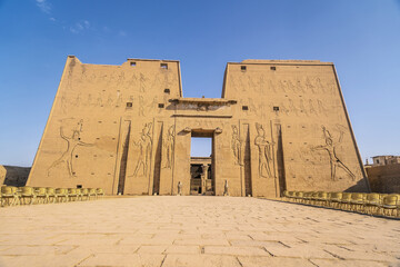 Facade with drawing of pharaohs of the Temple of Edfu in the city of Edfu, Egypt. On the bank of the Nile river, geco-Roman construction, temple dedicated to Huros - obrazy, fototapety, plakaty
