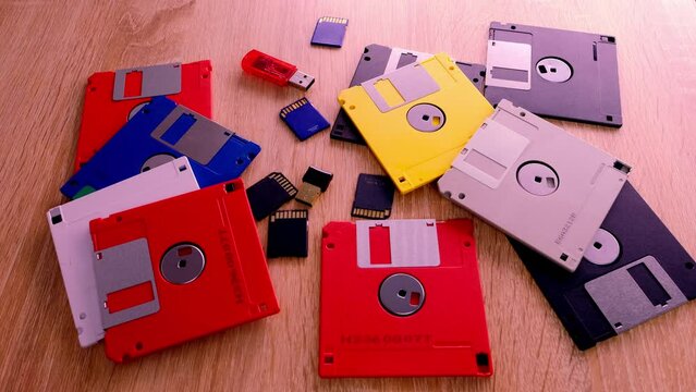 vintage retro electronic data storage devices from the 80s, 90s, cd disk, flash drives scattered on table. Stack of floppy disks, pendrive and hard disk in grey, black, blue, yellow, red, white