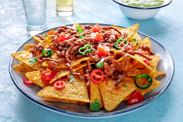 Nachos, Mexican food, tortilla chips with beef and fresh vegetables, with tequila, on a blue slate background