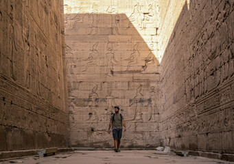 A young tourist visiting the beautiful temple of Edfu in the city of Edfu, Egypt. On the bank of the Nile river, geco-Roman construction, temple dedicated to Huros - obrazy, fototapety, plakaty