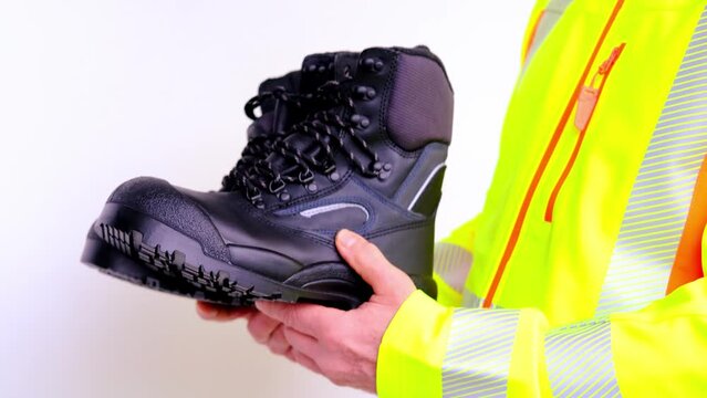 black work boots made of leather with reinforced cape, high top in hands of man, mature male mature builder, worker in yellow work clothes testing special protective professional shoes, for mountains