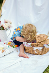 A child with curly hair looks into a picnic basket on a white blanket