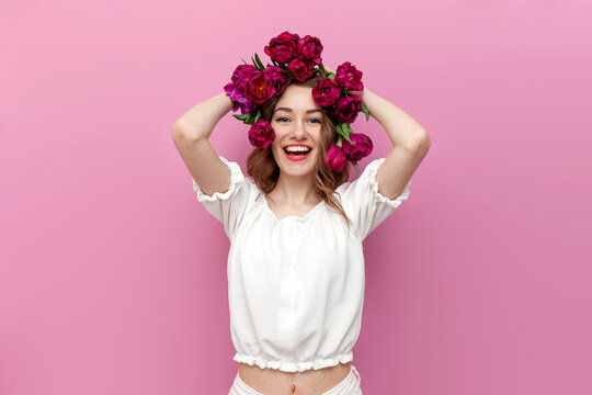 young tender girl with pink tulips in her hair smiles on pink isolated background, woman with flowers on her head