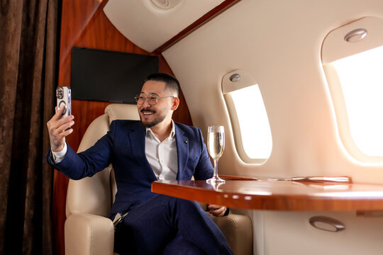 young asian businessman is sitting in private luxury jet and communicate via smartphone video call
